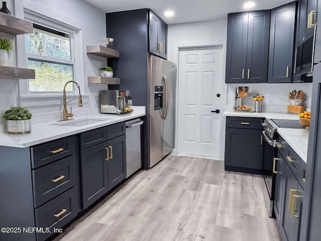 kitchen featuring light wood-style flooring, open shelves, a sink, appliances with stainless steel finishes, and light countertops