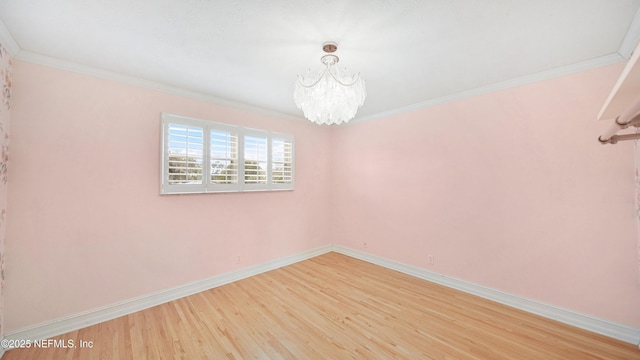 spare room featuring light wood finished floors, baseboards, a notable chandelier, and ornamental molding