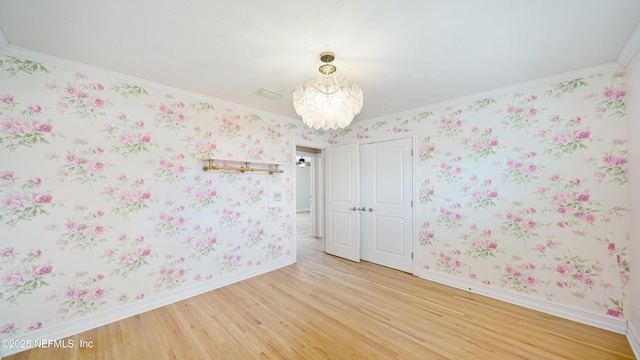 spare room featuring light wood-type flooring, a notable chandelier, baseboards, and wallpapered walls