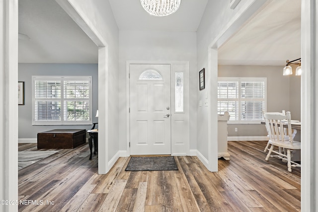 foyer entrance with baseboards, wood finished floors, a wealth of natural light, and an inviting chandelier