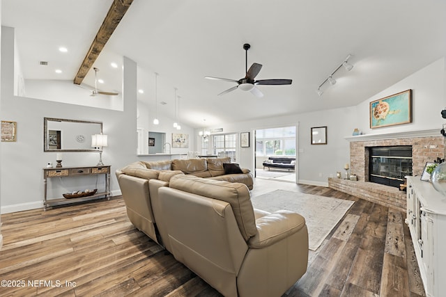 living area featuring a fireplace, vaulted ceiling with beams, a ceiling fan, wood finished floors, and baseboards