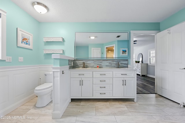 bathroom featuring double vanity, visible vents, toilet, a wainscoted wall, and a sink