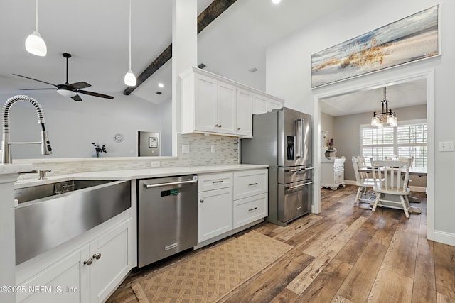 kitchen featuring light wood finished floors, backsplash, lofted ceiling with beams, appliances with stainless steel finishes, and a sink