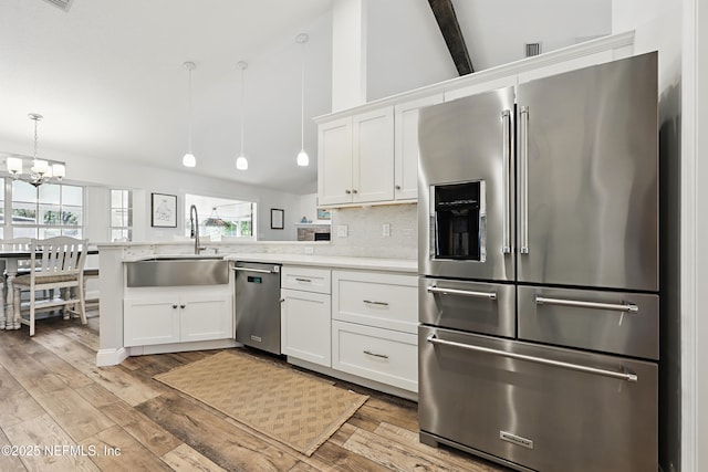 kitchen featuring stainless steel appliances, light countertops, white cabinets, a sink, and a peninsula