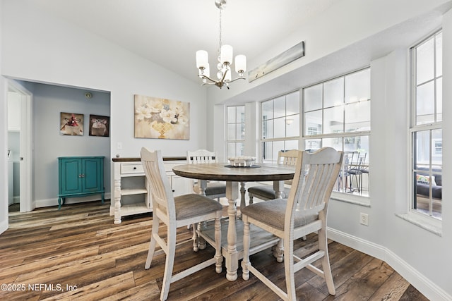 dining space featuring dark wood-type flooring, a chandelier, vaulted ceiling, and baseboards