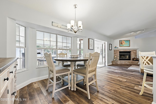 dining area with dark wood-style flooring, a fireplace, an inviting chandelier, vaulted ceiling, and baseboards