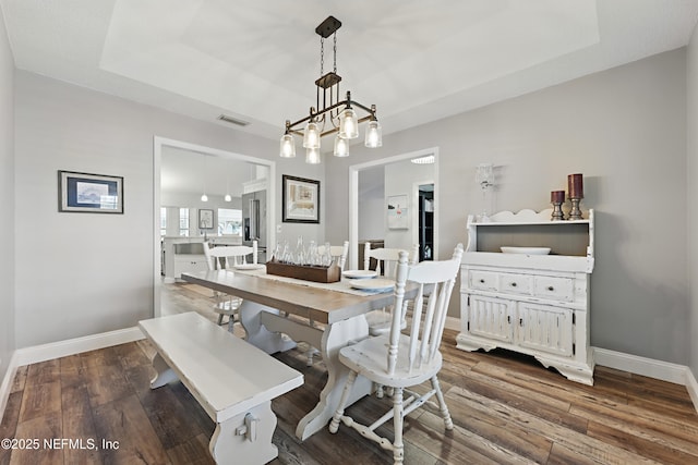 dining space with a notable chandelier, a raised ceiling, visible vents, dark wood-type flooring, and baseboards