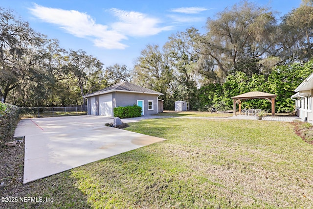 view of yard featuring a gazebo, a detached garage, fence, and an outbuilding