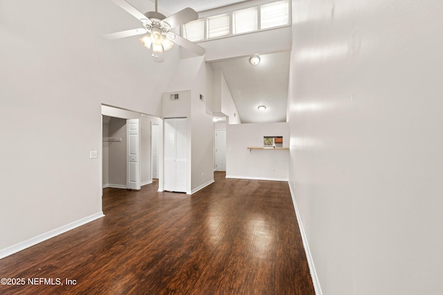 unfurnished living room with ceiling fan, a high ceiling, wood finished floors, visible vents, and baseboards