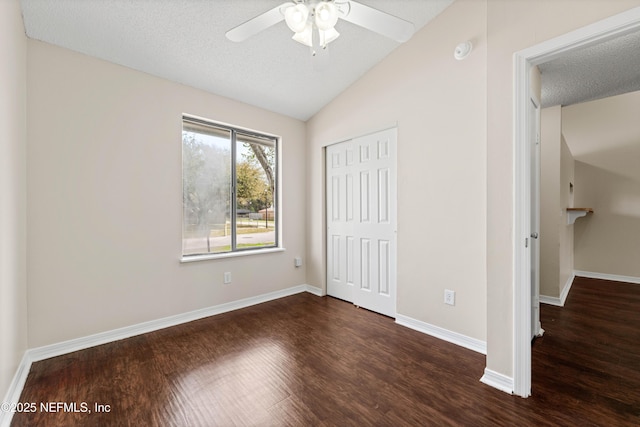 unfurnished bedroom with a textured ceiling, lofted ceiling, baseboards, a closet, and dark wood-style floors