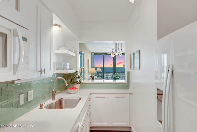 kitchen featuring white fridge with ice dispenser, backsplash, a sink, and white cabinets