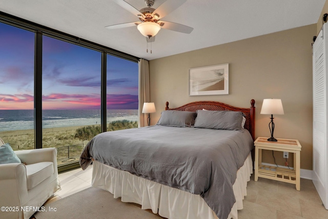 bedroom with a barn door, a beach view, a ceiling fan, a water view, and expansive windows