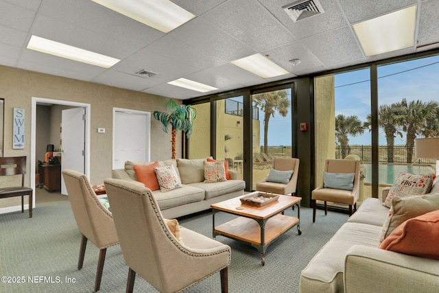 living area with a wall of windows, carpet, visible vents, and a drop ceiling