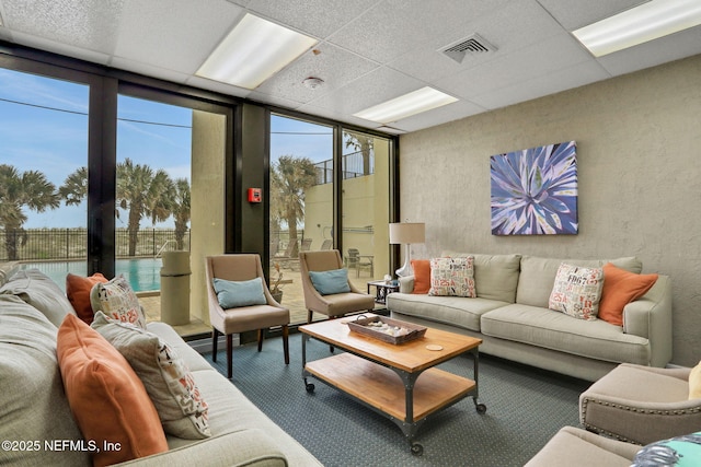 living room with a textured wall, a paneled ceiling, visible vents, and floor to ceiling windows