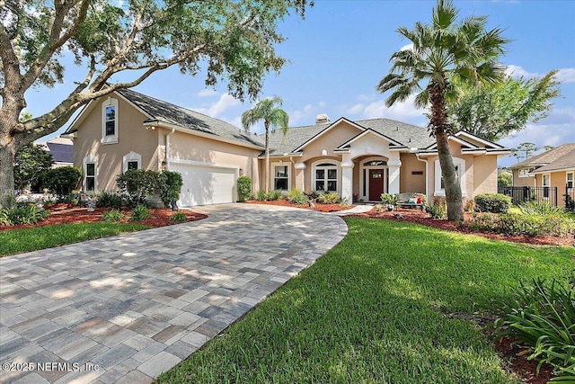 view of front of house with decorative driveway, stucco siding, a front yard, fence, and a garage