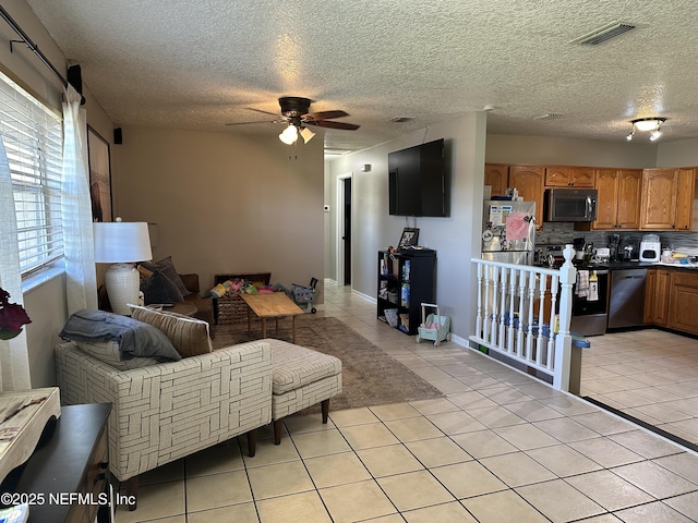 living area featuring light tile patterned flooring, ceiling fan, visible vents, and a textured ceiling