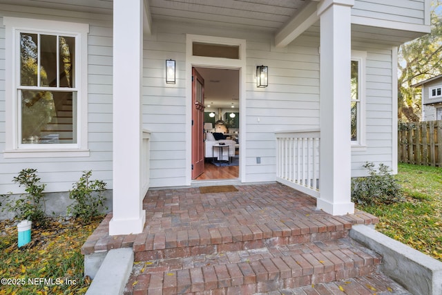 doorway to property with a porch and fence