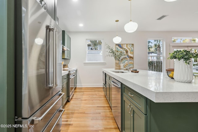 kitchen featuring high quality appliances, light wood-style flooring, a sink, green cabinets, and hanging light fixtures