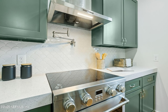 kitchen with light stone counters, extractor fan, stainless steel range, green cabinets, and tasteful backsplash