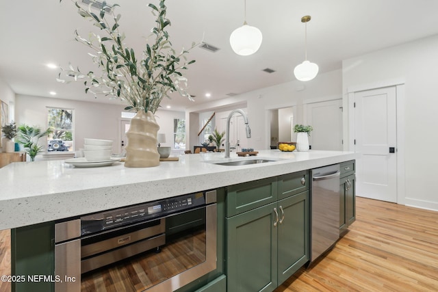 kitchen with light wood finished floors, visible vents, green cabinets, dishwasher, and a sink