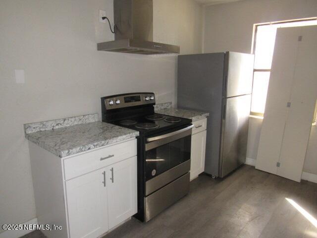 kitchen with light wood-type flooring, wall chimney exhaust hood, white cabinetry, and stainless steel appliances