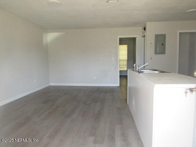 unfurnished room featuring light wood-style flooring, electric panel, baseboards, and a sink