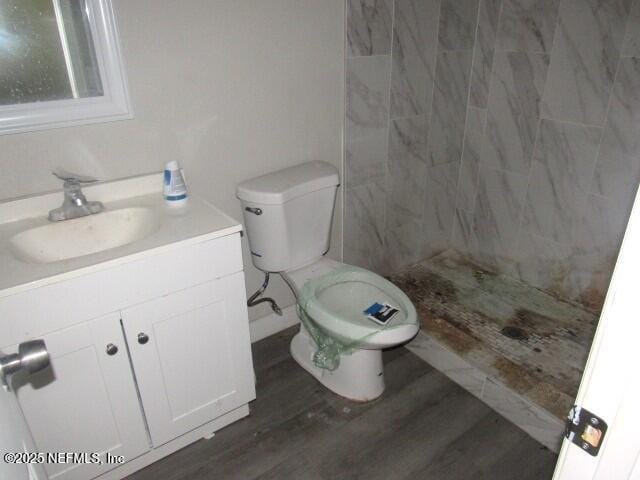 bathroom featuring toilet, tiled shower, wood finished floors, and vanity