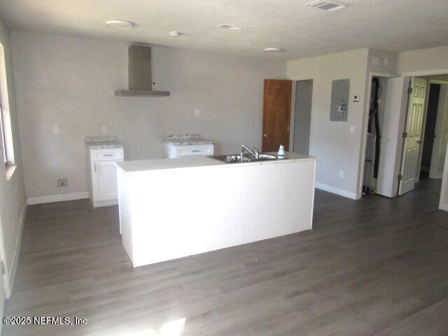 kitchen featuring wood finished floors, a sink, baseboards, white cabinets, and wall chimney exhaust hood