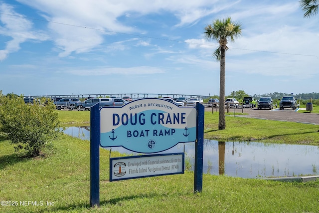 community / neighborhood sign featuring a water view, uncovered parking, and a yard