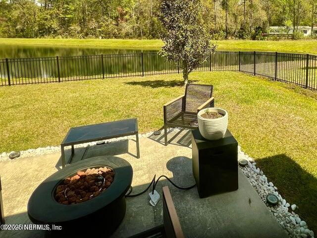 view of home's community with an outdoor fire pit, a fenced backyard, a water view, a patio area, and a lawn