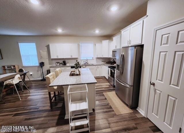 kitchen with a breakfast bar area, dark wood-style flooring, white cabinets, appliances with stainless steel finishes, and a center island