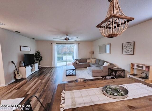 living area featuring visible vents, baseboards, wood finished floors, and ceiling fan with notable chandelier