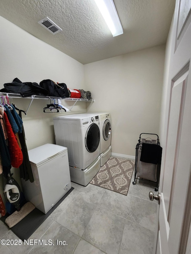 clothes washing area featuring visible vents, baseboards, laundry area, a textured ceiling, and separate washer and dryer