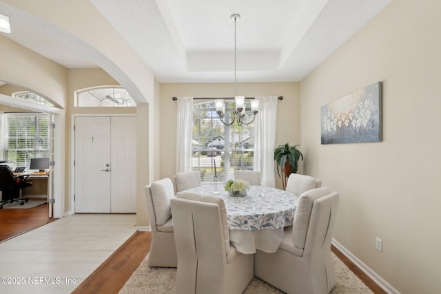 dining area featuring arched walkways, baseboards, a raised ceiling, wood finished floors, and an inviting chandelier