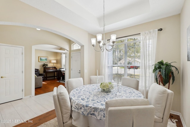 dining space featuring an inviting chandelier, a tray ceiling, arched walkways, and wood finished floors