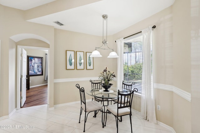 dining area featuring light tile patterned floors, baseboards, visible vents, and arched walkways