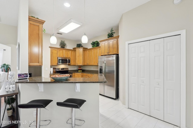 kitchen with decorative light fixtures, a breakfast bar area, stainless steel appliances, dark stone counters, and a peninsula