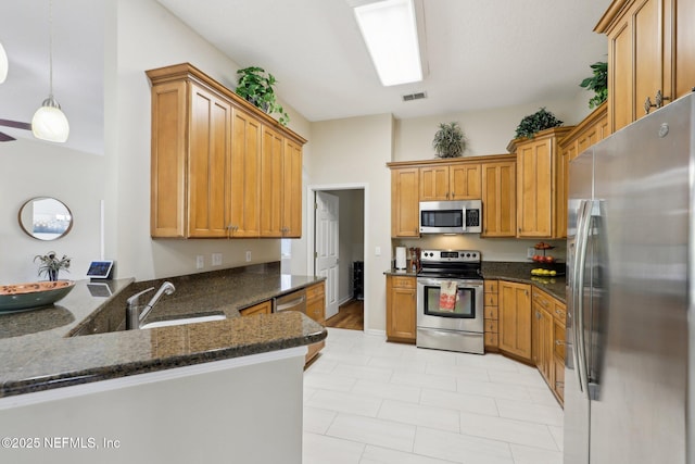 kitchen with visible vents, dark stone counters, a peninsula, stainless steel appliances, and a sink