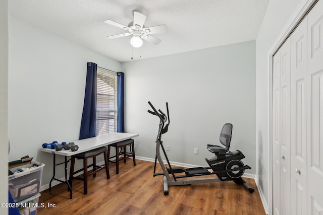 workout room featuring ceiling fan, a textured ceiling, baseboards, and wood finished floors