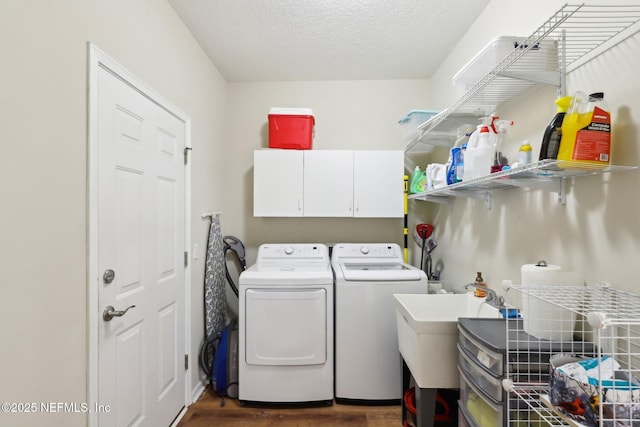 washroom featuring cabinet space, washer and clothes dryer, dark wood-type flooring, a textured ceiling, and a sink