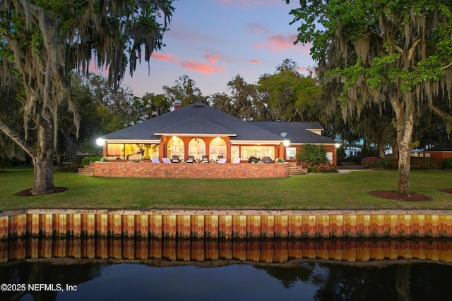 rear view of property featuring a chimney, a yard, and a water view