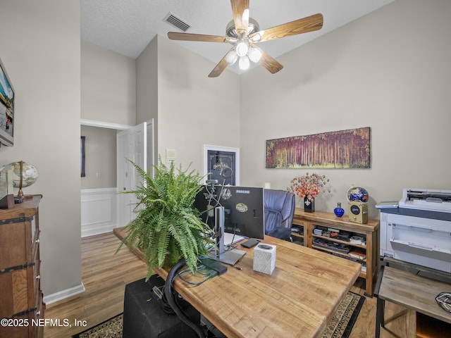 office area with visible vents, a wainscoted wall, a textured ceiling, wood finished floors, and ceiling fan