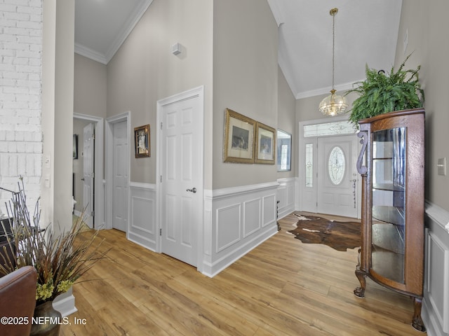 entryway with light wood-type flooring, a notable chandelier, wainscoting, and crown molding