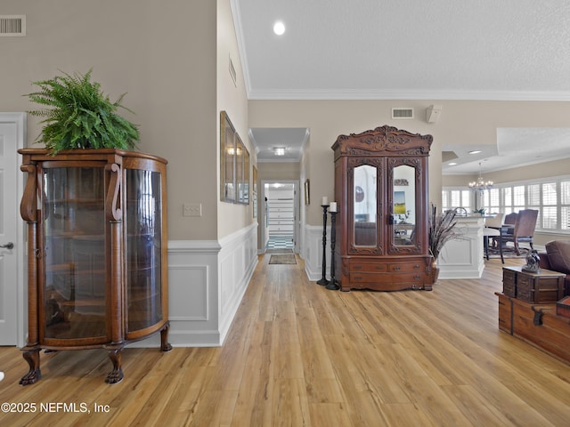 foyer with a wainscoted wall, light wood-style floors, visible vents, and ornamental molding