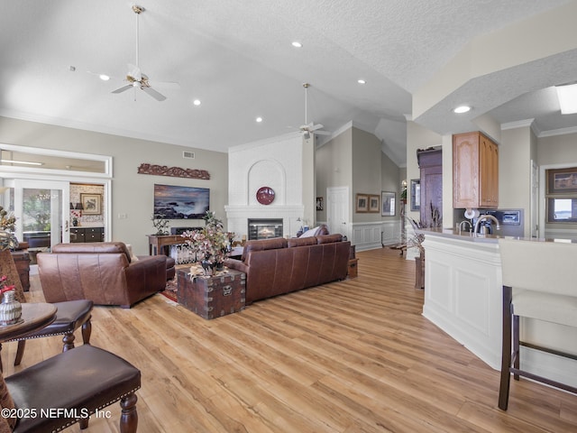 living area featuring light wood finished floors, crown molding, a fireplace, a textured ceiling, and a ceiling fan