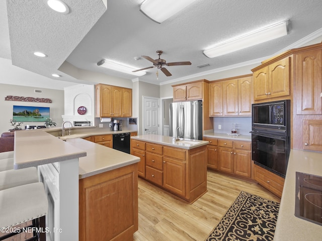 kitchen featuring a peninsula, a kitchen island with sink, black appliances, light countertops, and light wood-style floors