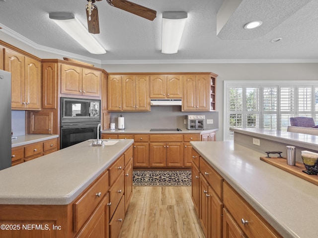 kitchen featuring ornamental molding, a sink, black appliances, light countertops, and under cabinet range hood