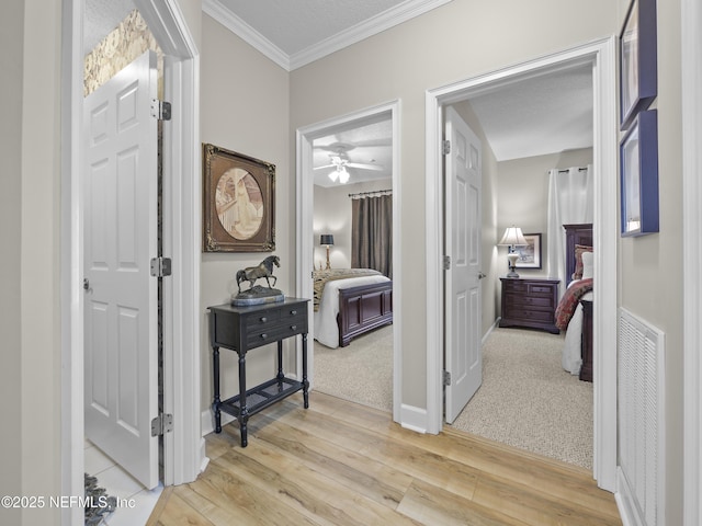 corridor with visible vents, light wood-style flooring, baseboards, and ornamental molding