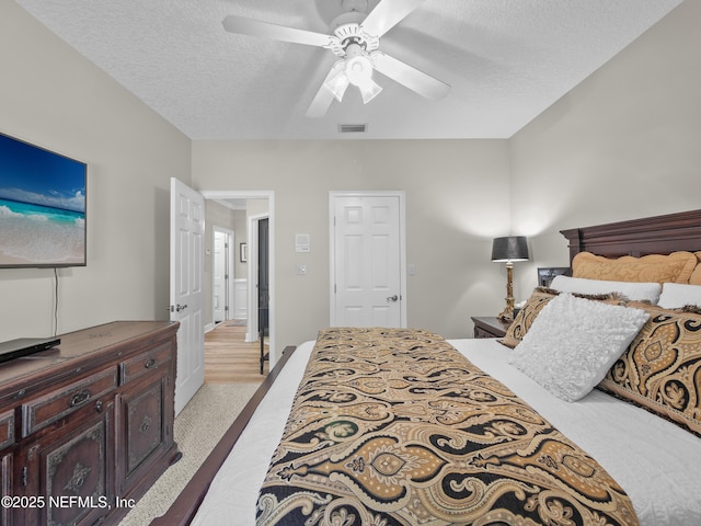 bedroom with ceiling fan, light colored carpet, visible vents, and a textured ceiling