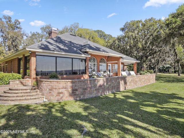 back of property with a yard, brick siding, a chimney, and a shingled roof